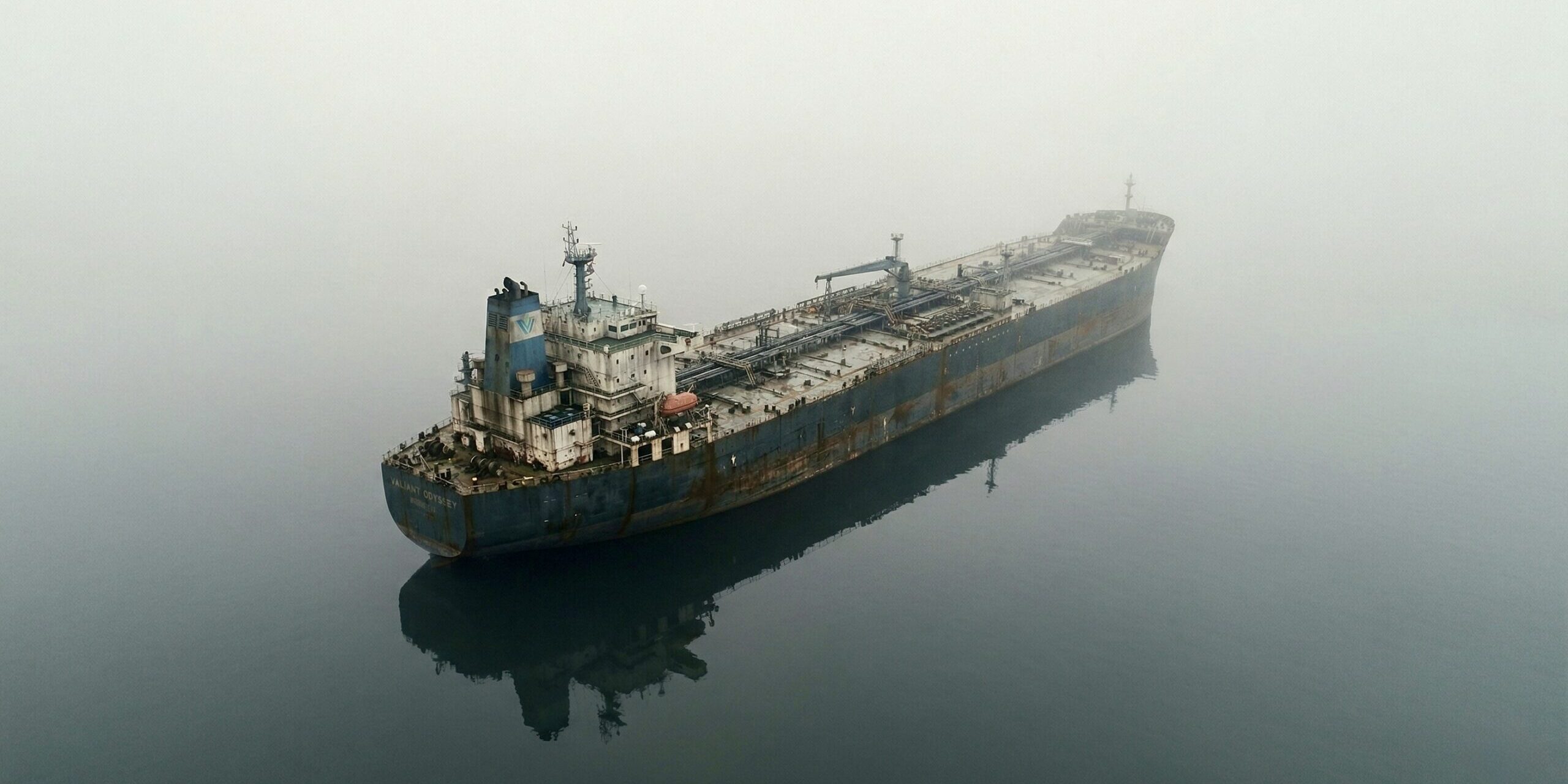 Q1 2026 Fog of War Aerial view of a massive cargo tanker drifting through dense fog on a still, glassy sea — illustrating the geopolitical supply chain uncertainty described in Riverwater Partners' Q1 2026 quarterly letter.