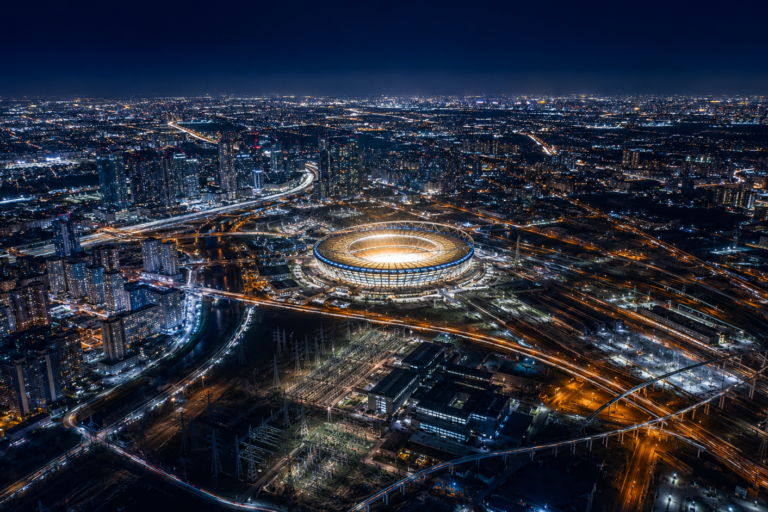 Aerial night view of a brightly lit stadium at the center of a sprawling, illuminated city grid
